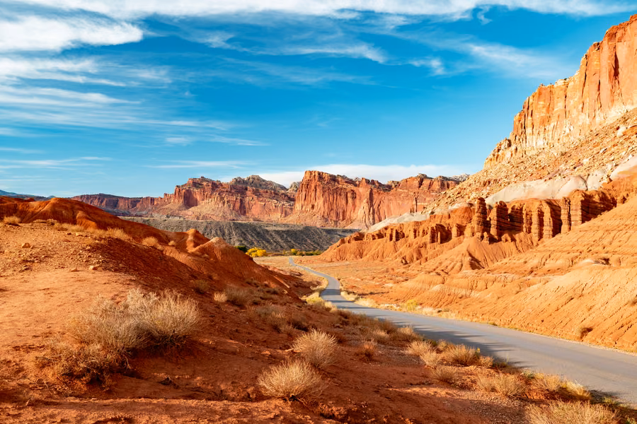 Road winding past layered red and cream cliffs under a blue sky in Capitol Reef National Park