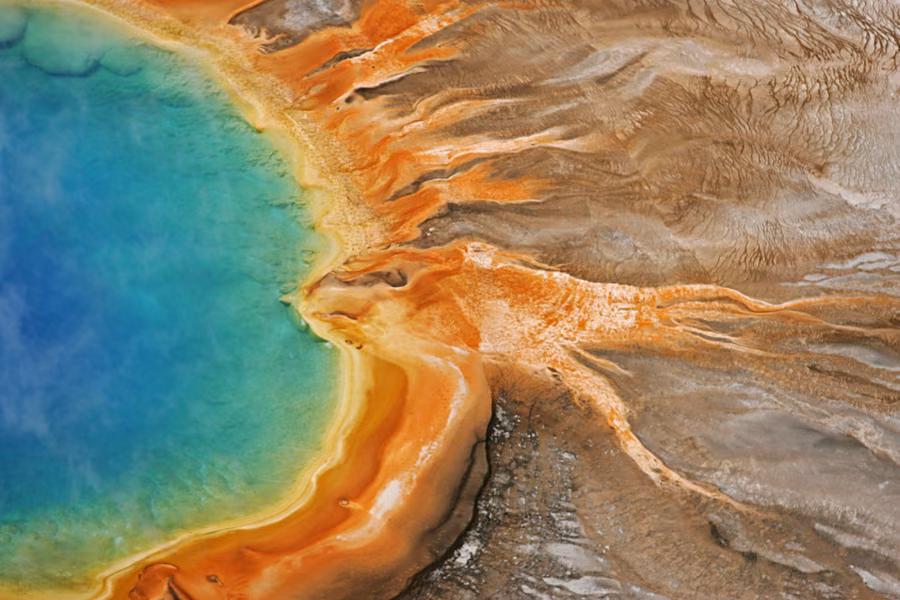 Aerial view of a vivid blue hot spring ringed by orange bacterial mats in Yellowstone National Park