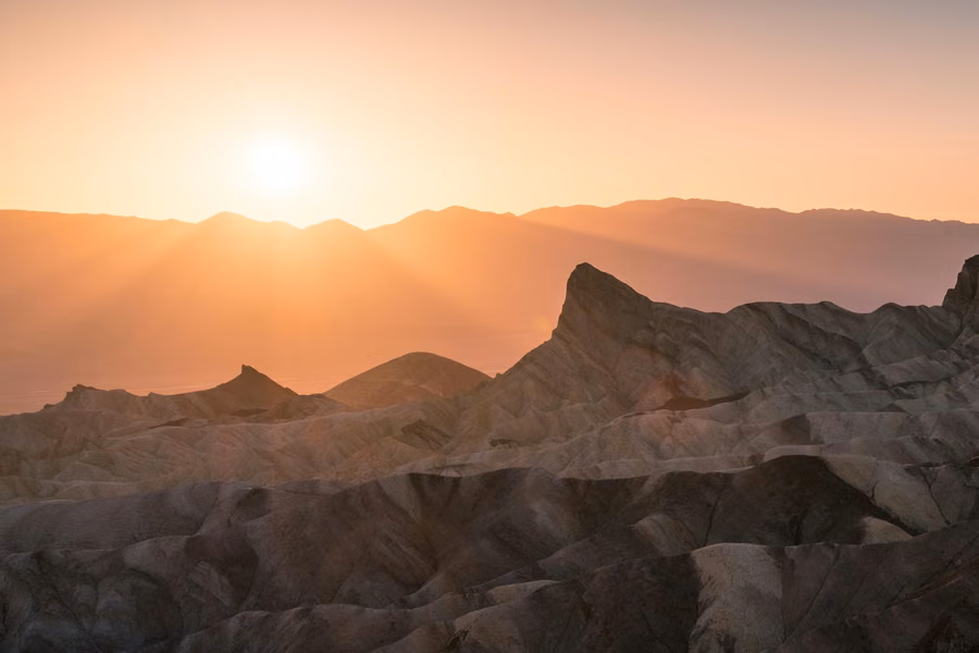 Sun setting behind mountain ridges above the eroded badlands of Death Valley National Park