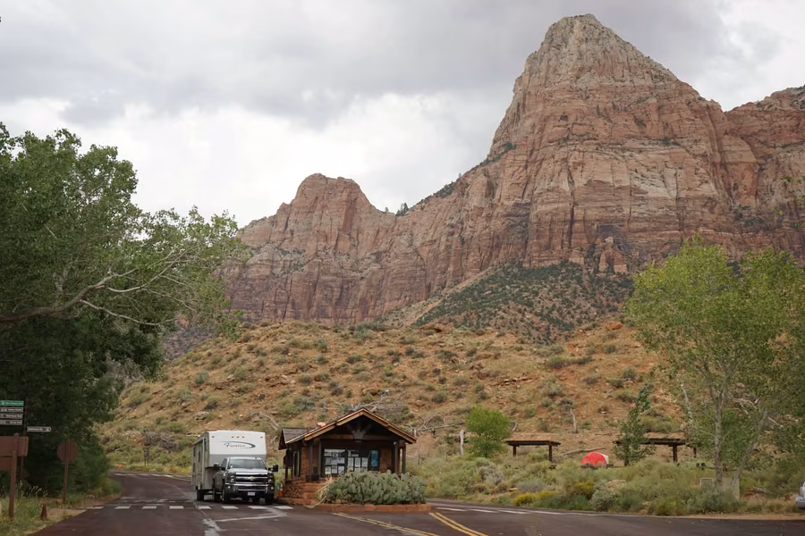 Pickup towing a travel trailer at the Watchman Campground entrance kiosk below Bridge Mountain in Zion National Park