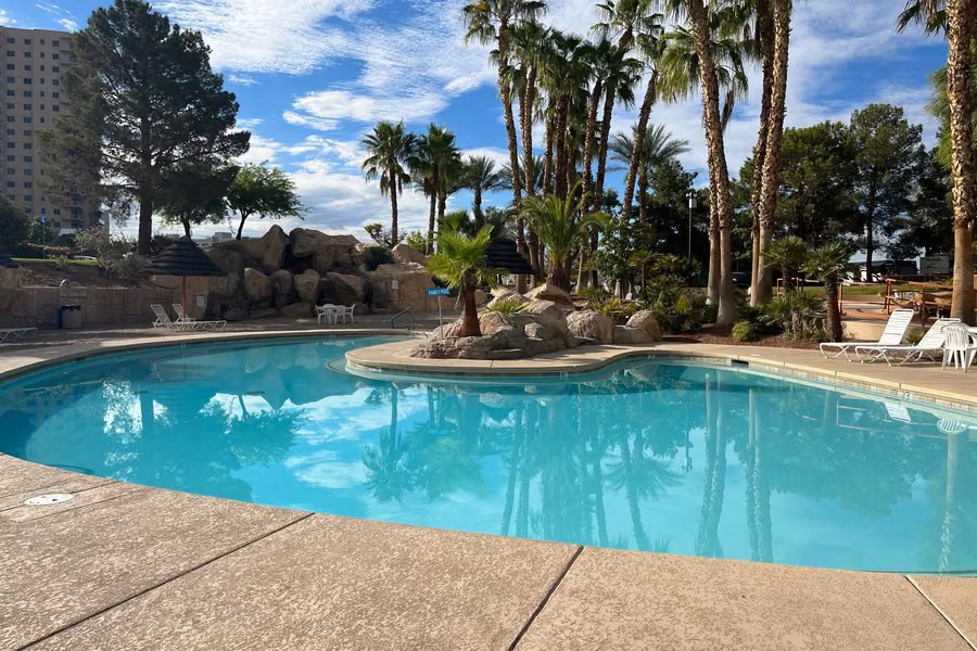 Lagoon-style swimming pool with a rock island, palm trees and sun loungers at Oasis Las Vegas RV Resort