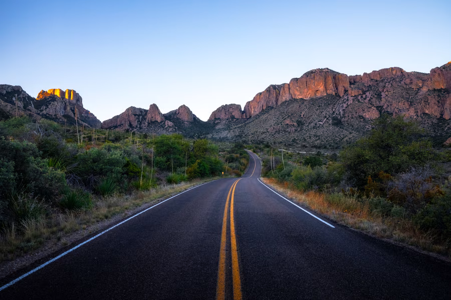 Empty two-lane road leading towards rugged, sunlit peaks in Big Bend National Park