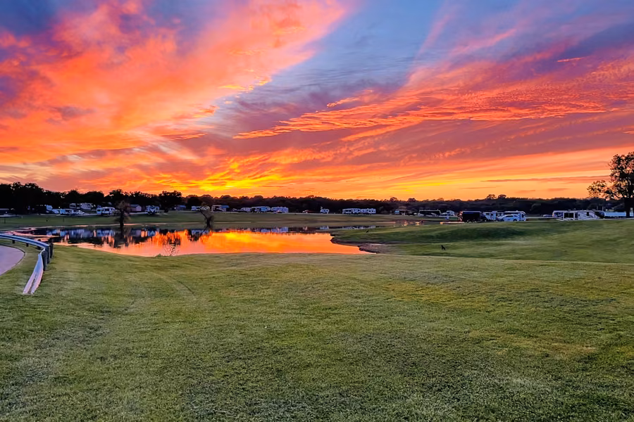 Fiery sunset over Grapevine Lake, with RVs lined up along the shore at The Vineyards Campground
