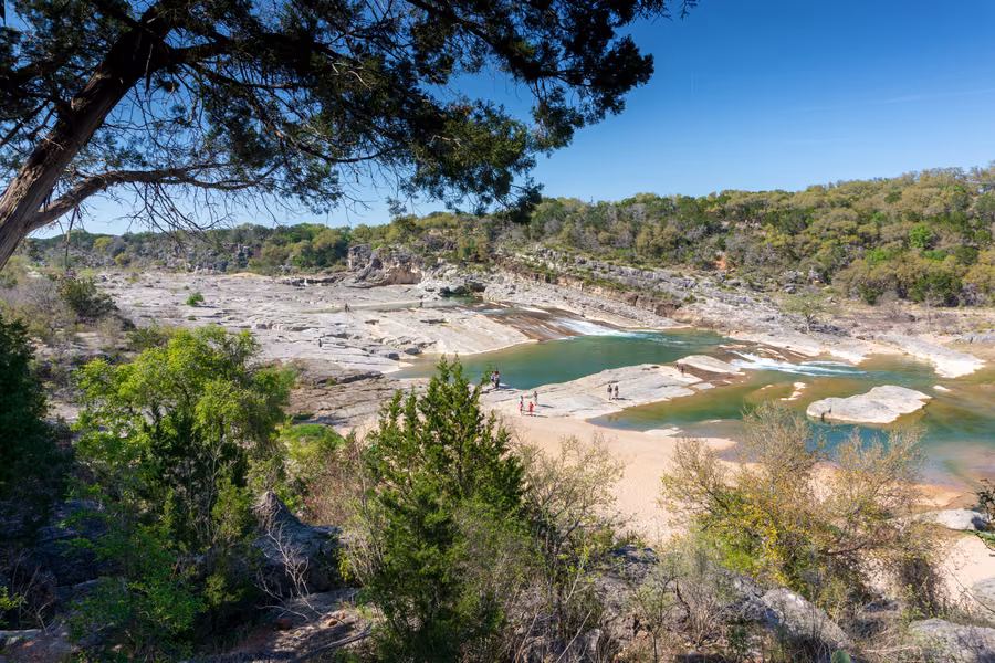 Pedernales River spilling over tiers of pale limestone into green pools at Pedernales Falls, framed by trees