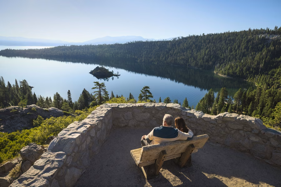 Couple on a bench at a stone lookout above Emerald Bay and Fannette Island at Lake Tahoe