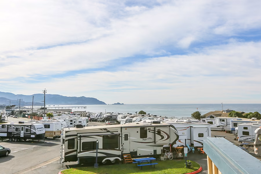 Rows of RVs and fifth wheels parked at San Francisco RV Resort in Pacifica, with the Pacific Ocean and Pacifica Pier behind