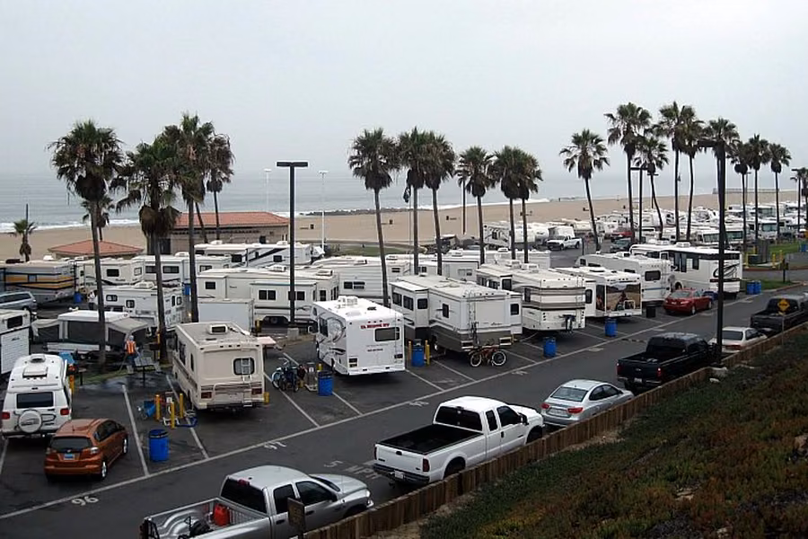 Motorhomes and trailers parked in rows under palm trees at Dockweiler Beach RV Park, with the beach and ocean behind