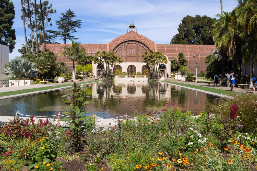The Botanical Building in Balboa Park reflected in its lily pond, framed by palms and flowering gardens