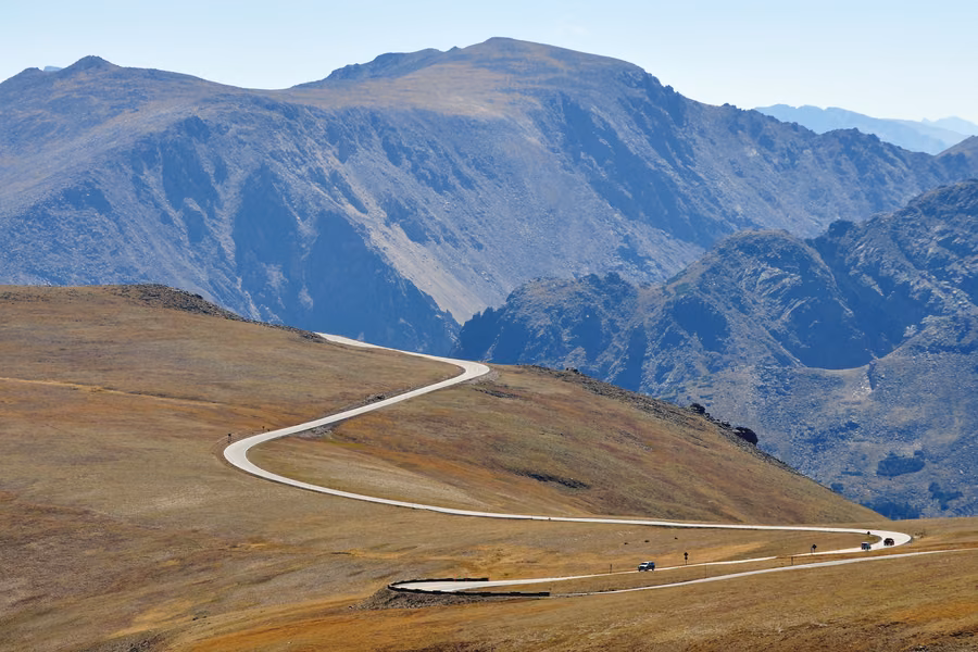 Trail Ridge Road winding across golden alpine tundra in Rocky Mountain National Park, with a few cars below rocky peaks