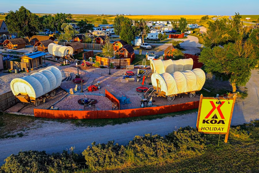 Aerial view of Denver East / Strasburg KOA Holiday at sunset, with covered wagons, cabins, RVs and the yellow KOA Holiday sign