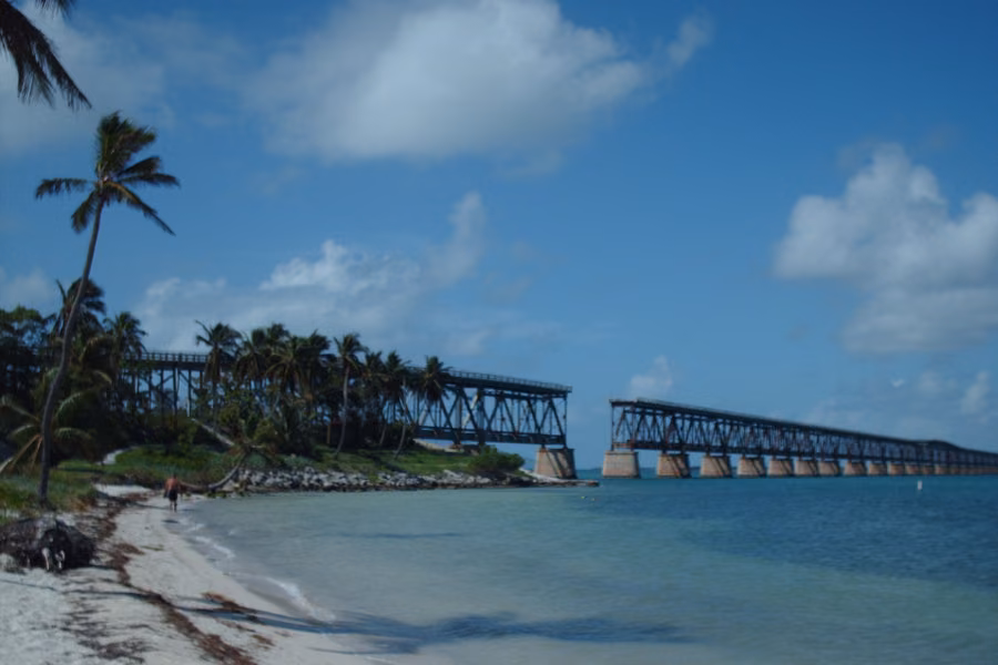 Palm-fringed beach and calm turquoise water at Bahia Honda State Park, with the old Bahia Honda Bridge spans behind