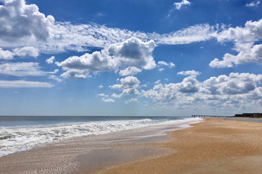 Wide sandy beach and rolling surf under a blue sky with white clouds at Anastasia State Park, St Augustine
