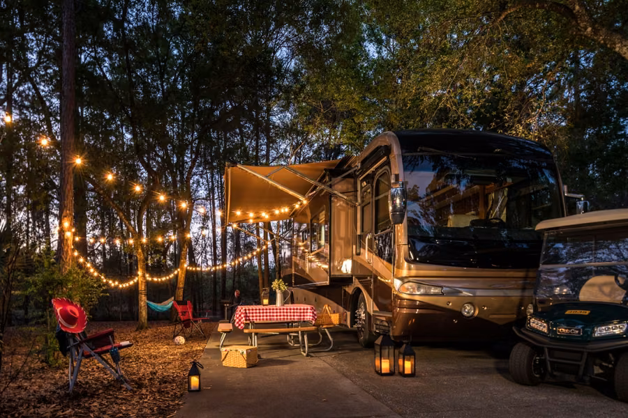 Motorhome with its awning out under string lights at a wooded campsite at Disney's Fort Wilderness Resort at dusk