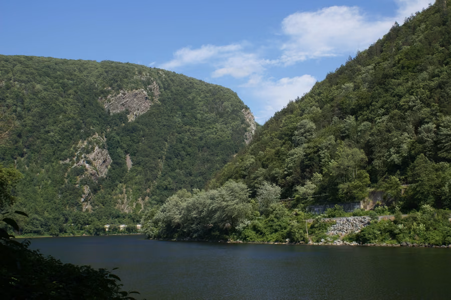 The Delaware River flowing between two steep forested mountains at the Delaware Water Gap under a blue sky