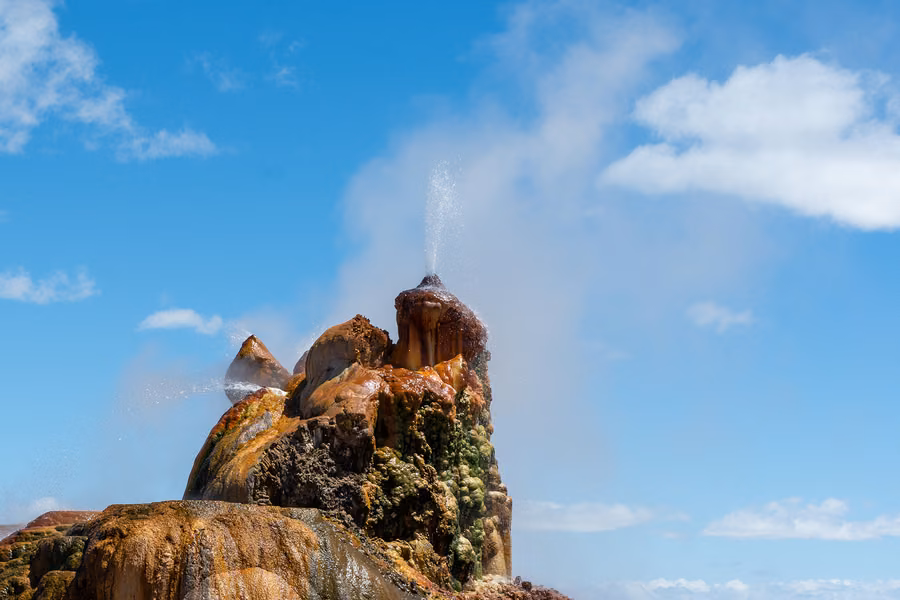 Fly Geyser, a coloured tufa mound with a thin jet of water and steam against a blue sky