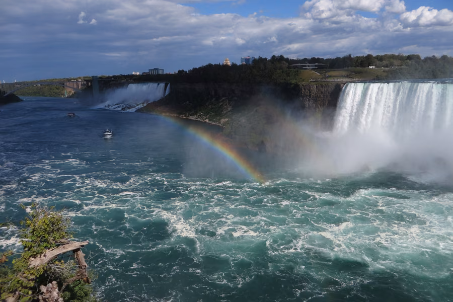 Rainbow over the churning Niagara River below the Horseshoe Falls, with the American Falls, the Rainbow Bridge and tour boats in the distance