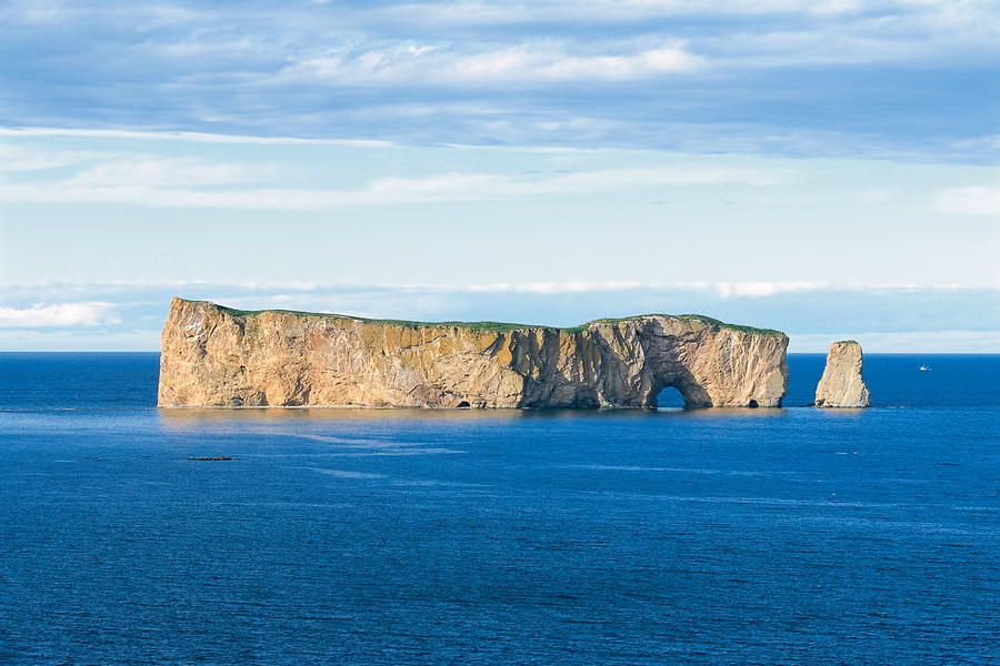 Percé Rock, with its sea arch and a smaller stack, rising from deep blue water off the Gaspé Peninsula under a summer sky