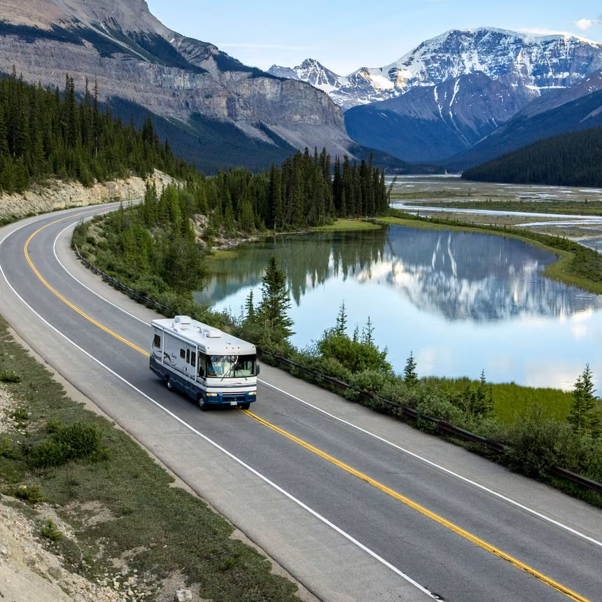 Motorhome driving the Icefields Parkway past a still river pool reflecting snow-capped peaks near Beauty Flats in Jasper National Park