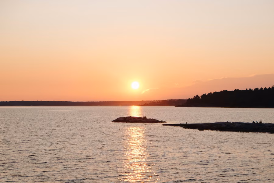 Sun setting over Georgian Bay at Killbear Provincial Park, with a low rocky island and the granite shoreline in silhouette