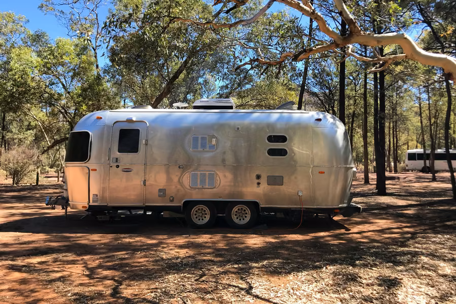 Silver Airstream caravan on a red dirt site under gum trees at the Wilpena Pound campground in the Flinders Ranges