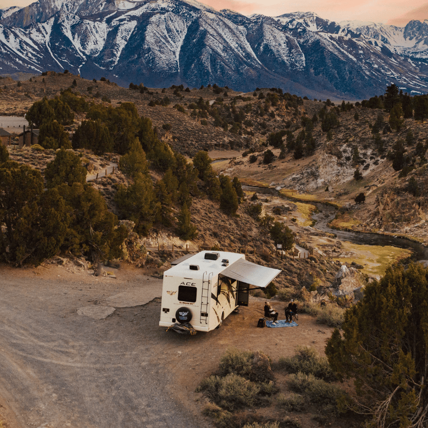 Campervan parked at a scenic mountain campsite in the USA at sunset, surrounded by rugged terrain and snow-capped peaks — showcasing the freedom and adventure of campervan rentals for road trips and RV travel across America.