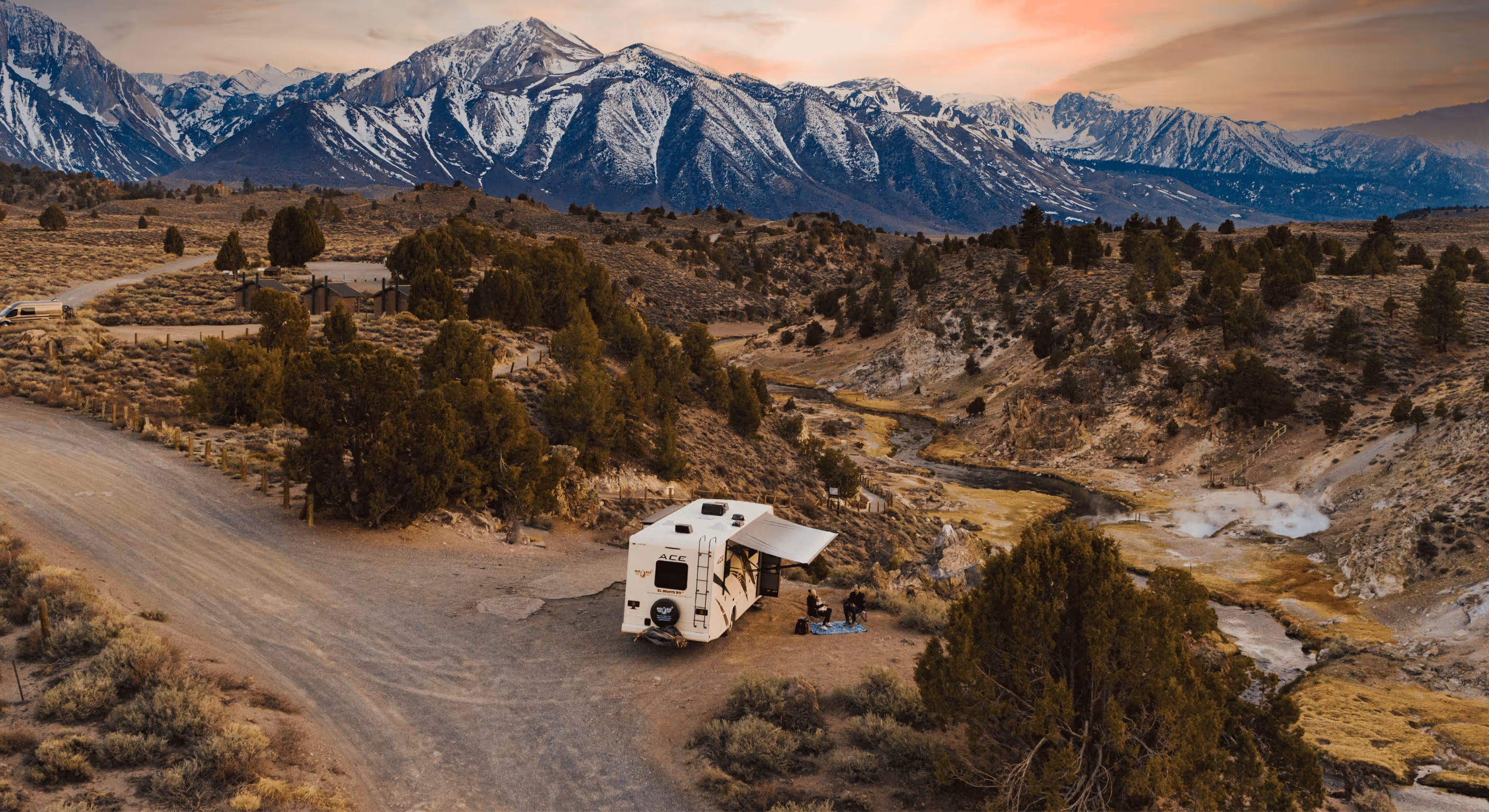 Campervan parked at a scenic mountain campsite in the USA at sunset, surrounded by rugged terrain and snow-capped peaks — showcasing the freedom and adventure of campervan rentals for road trips and RV travel across America.