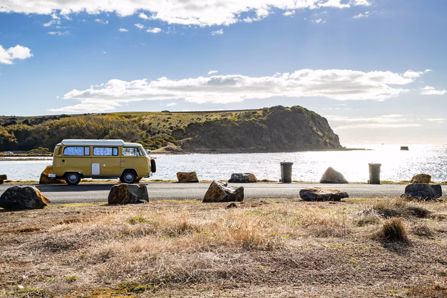 Yellow campervan parked beside a calm coastal inlet and headland in Tasmania