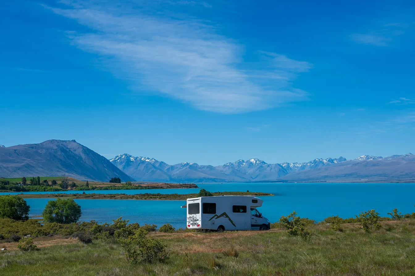 Self-contained motorhome parked beside Lake Tekapo with the Southern Alps behind, New Zealand