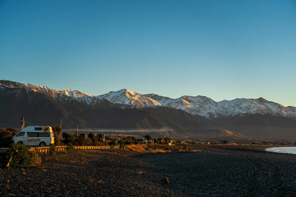 Campervan parked on the Kaikoura coast at sunset with the Seaward Kaikoura Range behind