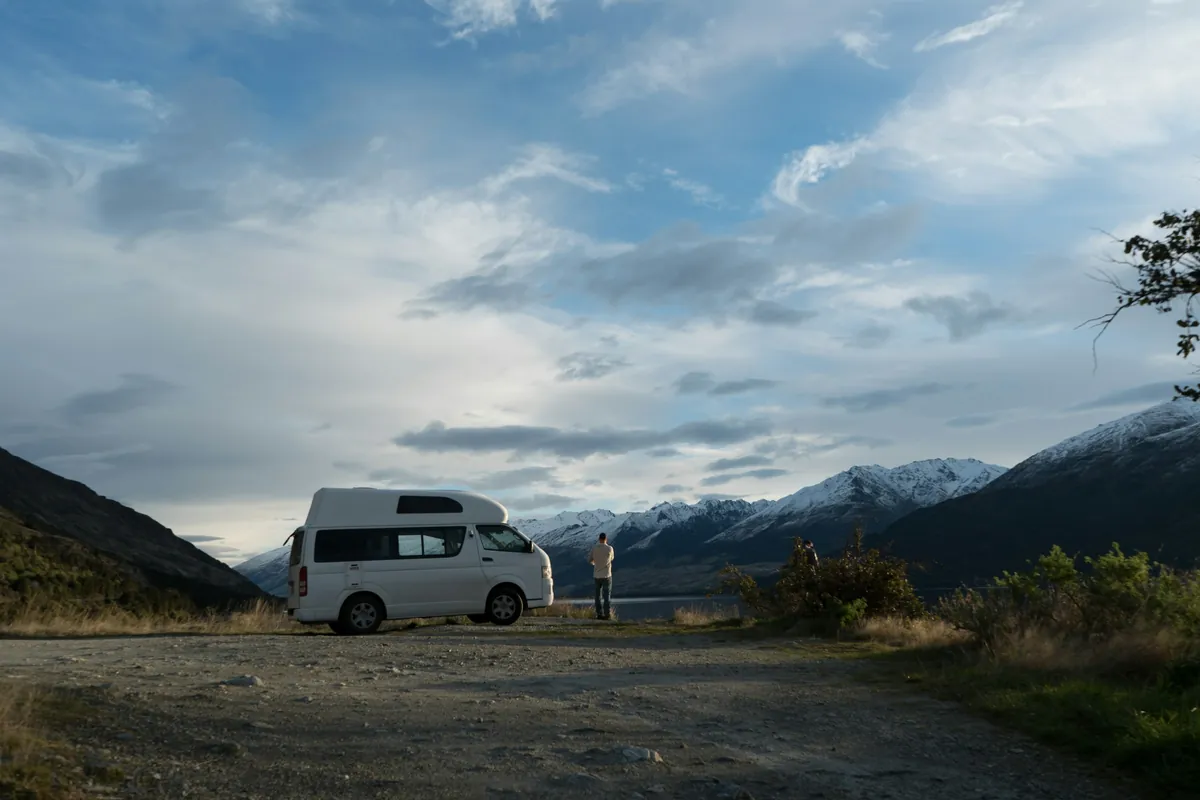 Campervan stopped at a gravel roadside pull-off with snowy mountains in New Zealand
