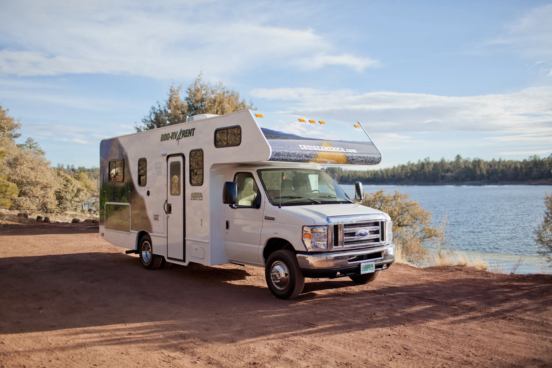 Cruise America RV parked beside a forest-lined lake