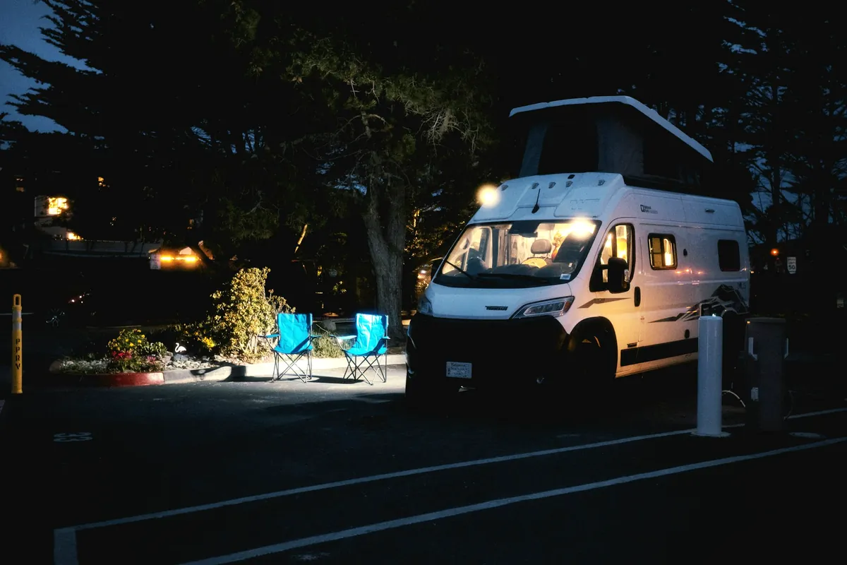 Pop-top campervan parked on a powered site at night next to the power pillar