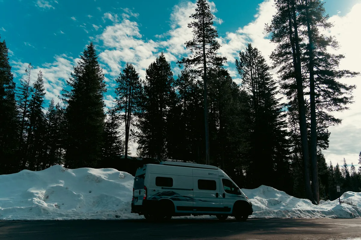 Campervan parked beside a snowy forest road with tall pine trees