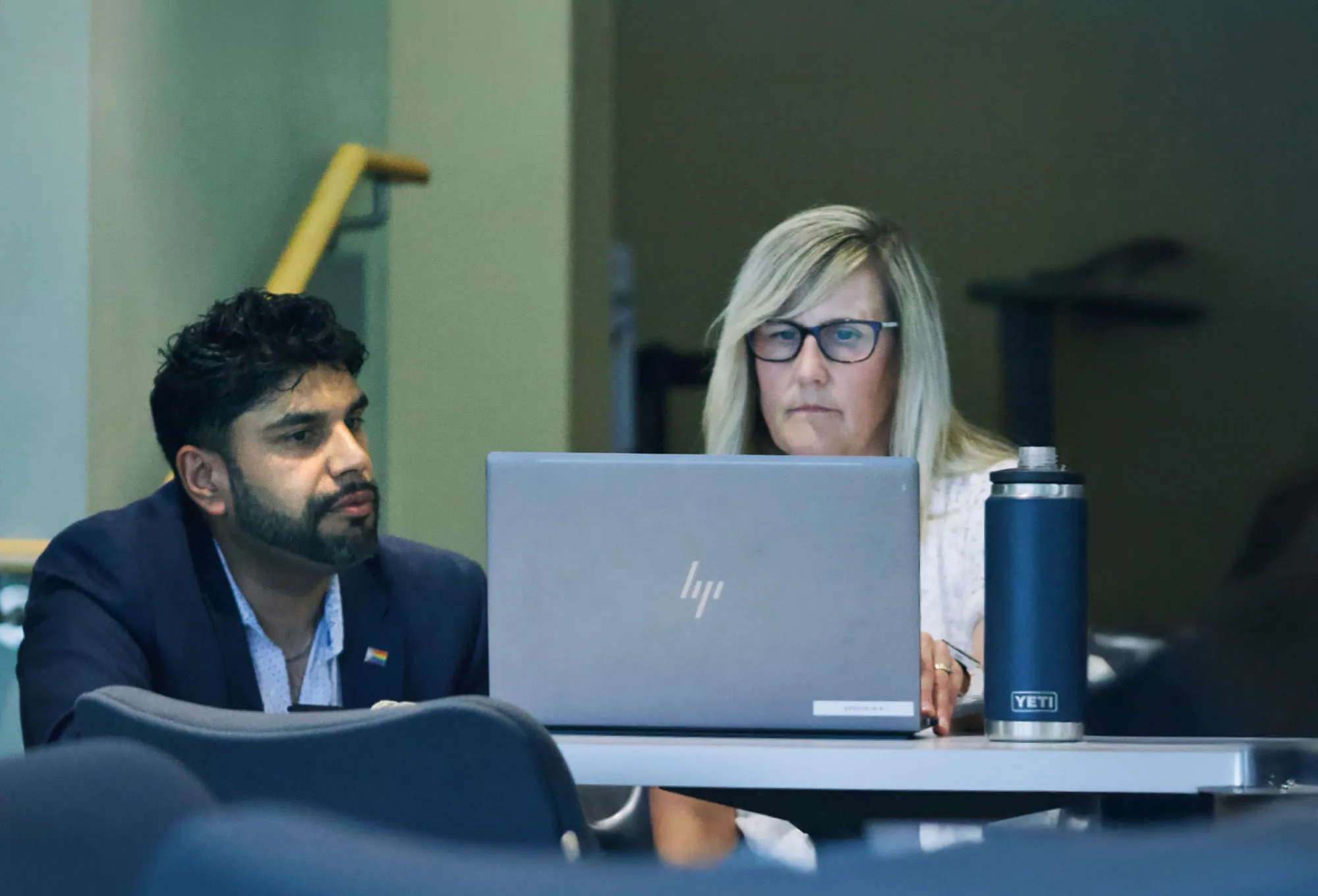 Two people working together at a laptop on a white table, with a blue Yeti water bottle beside them.