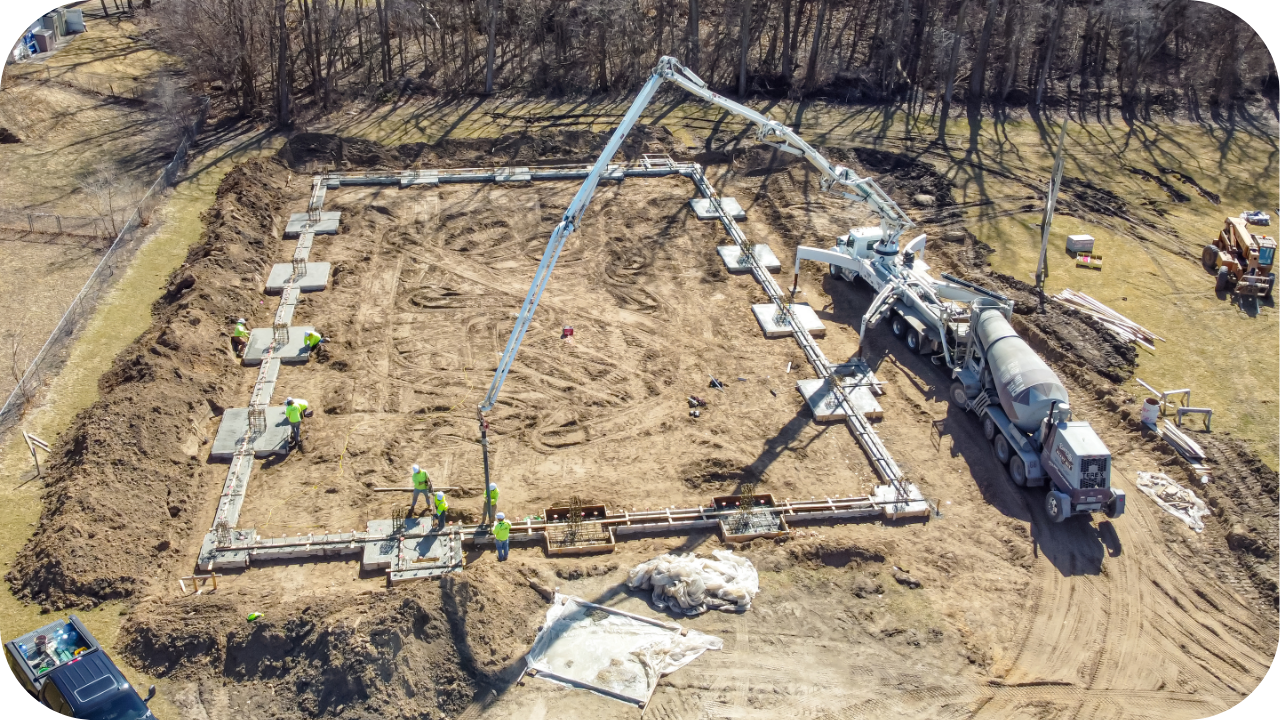 An aerial view of a construction site where a concrete boom pump is pouring the foundation footings for a new building.