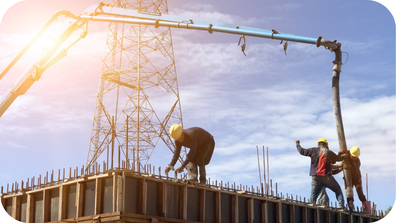 Construction workers pour a concrete wall formwork under a pump boom, with a large electrical tower in the background.