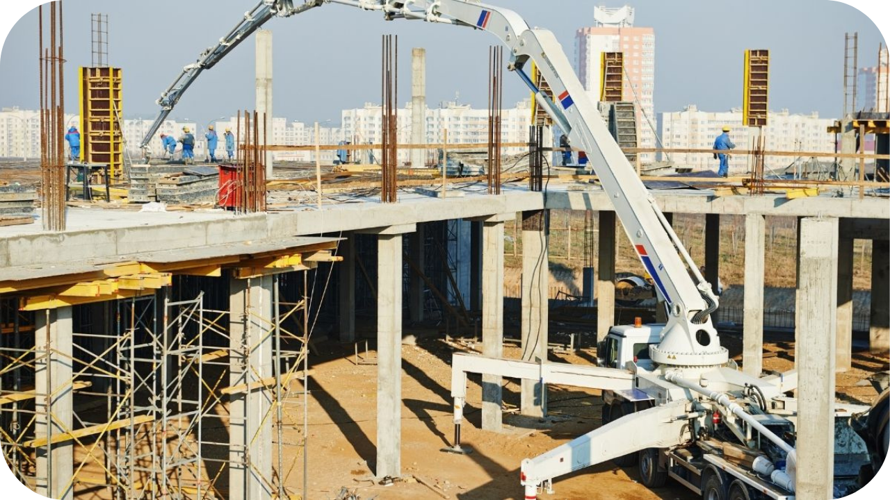 A concrete boom pump on a lower level of a construction site extends its long arm to pour the second-story floor of a new building.