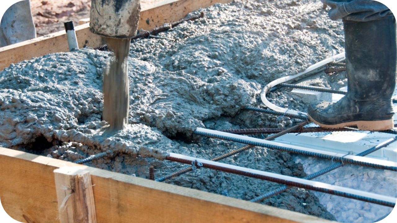 Wet concrete is poured from a pump hose into a wooden formwork, filling up around the steel rebar grid inside.