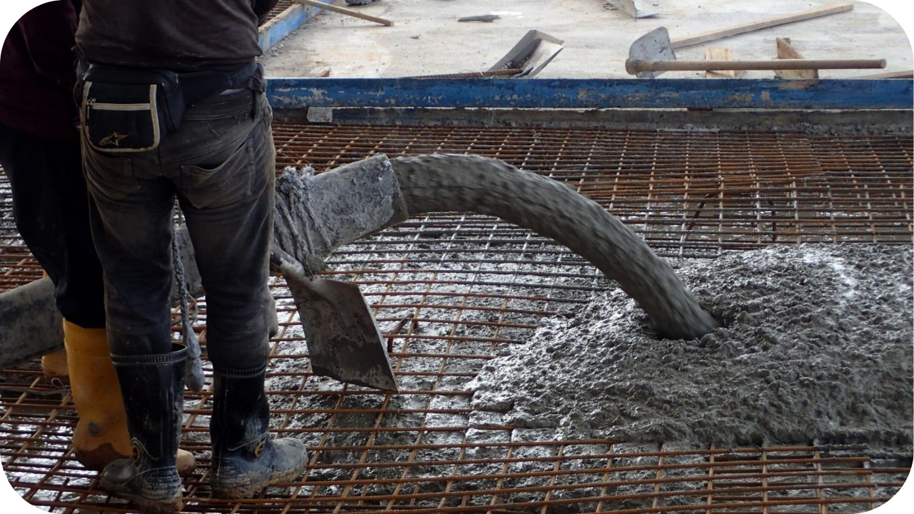 Workers guide a large, flexible hose as it pours wet concrete onto a dense grid of steel rebar for a new slab.