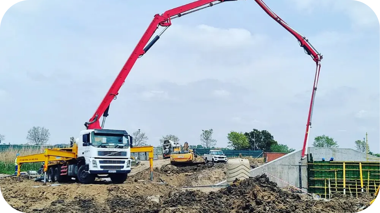 Concrete boom pump truck with extended arm pouring concrete at a construction site foundation.