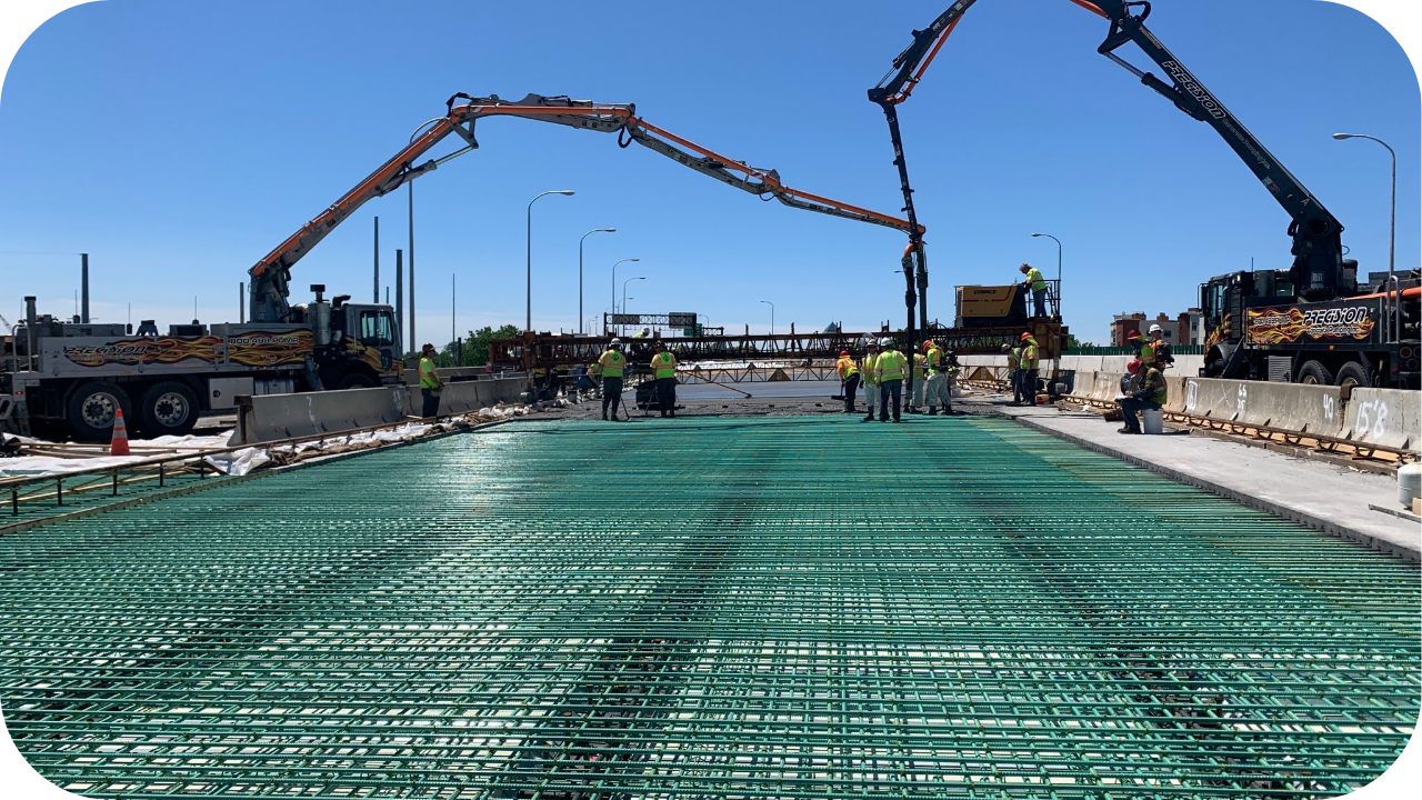 Construction workers using boom pump trucks to pour concrete on a reinforced bridge deck.
