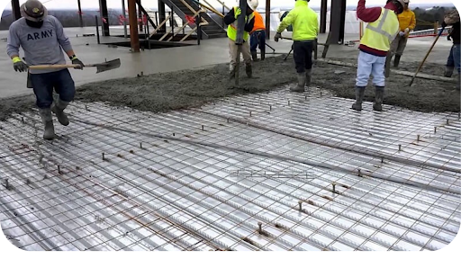 Concrete boom pump pouring slab on elevated construction site with workers spreading concrete across large foundation area.