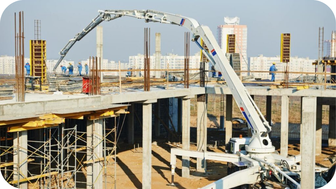 A concrete boom pump on a lower level of a construction site extends its long arm to pour the second-story floor of a new building.