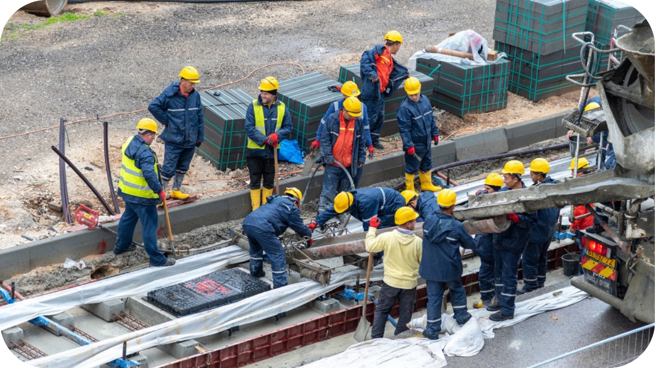 A high-angle view of a large construction crew in yellow hard hats working together around a concrete pour.
