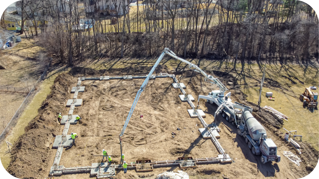 Aerial view of a concrete boom pump truck pouring foundation with workers at the construction site.