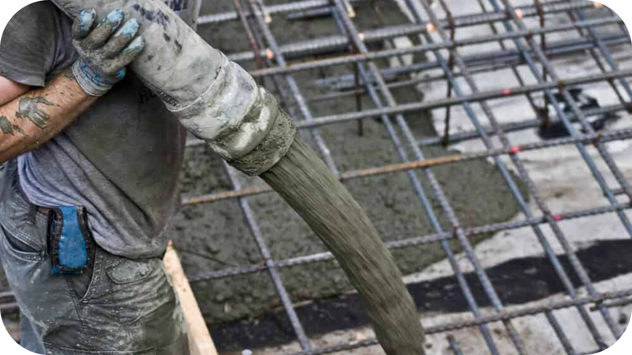 Close-up of wet concrete flowing from a pump hose onto a reinforced slab, guided by a worker in construction clothing.