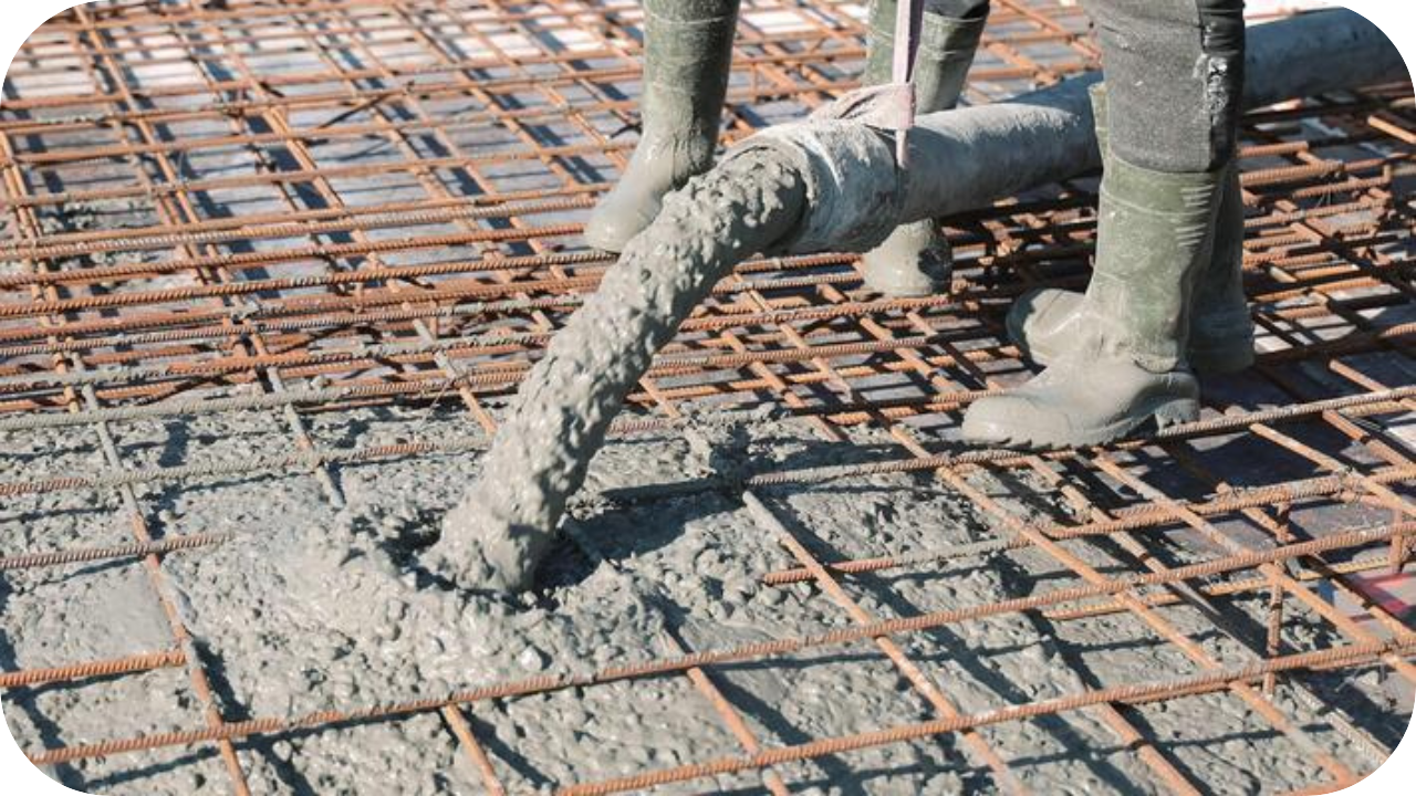 A close-up of concrete pouring through a line pump hose onto steel reinforcement mesh, with workers in boots guiding the flow.