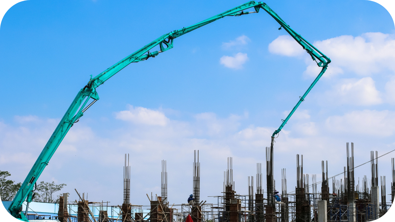 Green boom pump truck pouring concrete into tall column formwork at a construction site with scaffolding and workers in helmets.
