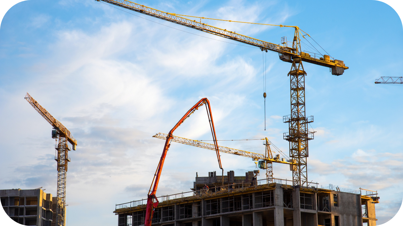 Red boom pump working on a tall building site with multiple cranes in the background under a blue sky.