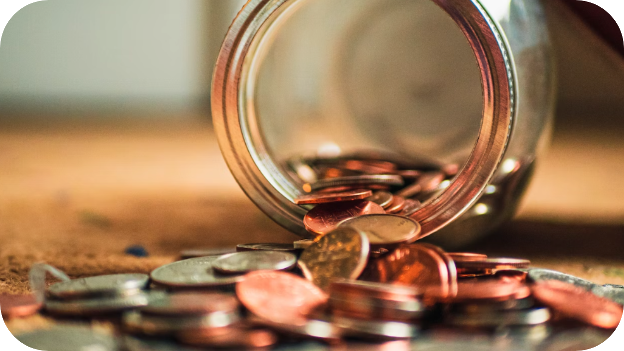 Coins spill from a glass jar onto a wooden surface, symbolising savings, affordability, and cost-effectiveness in concrete pumping services.